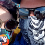 A couple, both wearing colourful face coverings and sunglasses